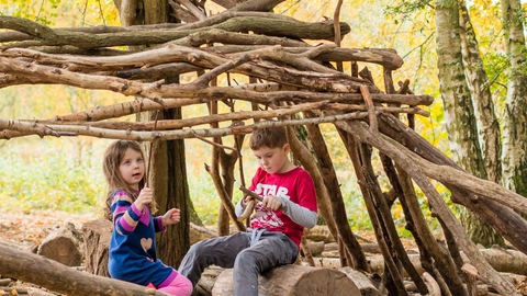 A girl and a boy playing in a den made of sticks