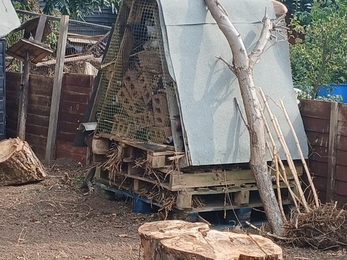 A bug hotel constructed of a pile of pallets stuffed with straw, old bricks and an angled roof cover.