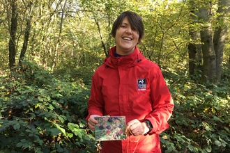 Vicky Dunne in a red coat holding up a photograph of berries