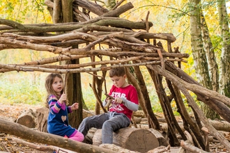 A girl and a boy playing in a den made of sticks