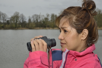 Woman birdwatching with binoculars by a lake