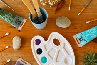 Photo of painting equipment: paint, palette, and paintbrushes with flowers and leaves