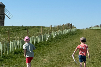 two boys running through a field towards a windmill
