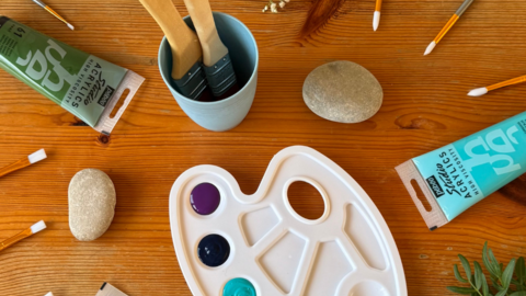 Photo of painting equipment: paint, palette, and paintbrushes with flowers and leaves