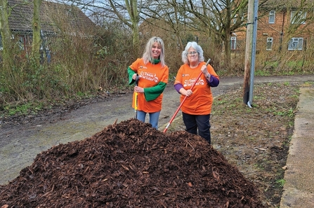 Two volunteers with a pile of wood chip.