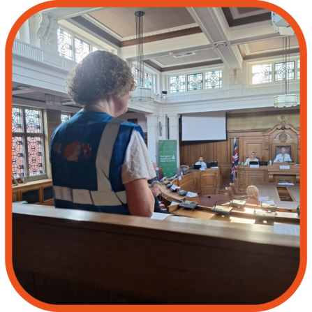 member of attelborough wildlife watchers addressing a county council cabinet meeting, wearing a blue hi vis with a hedgehog on the back