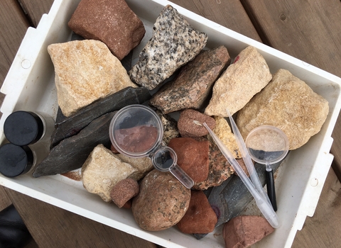 Tray of rocks on picnic table with magnifying glass