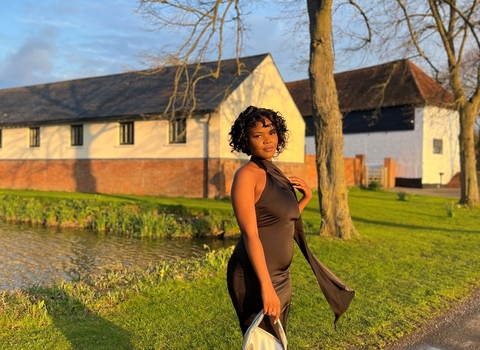 A woman in a fancy black dress poses by a tree with a silver handbag