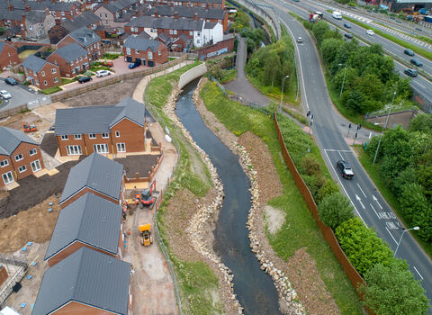 A restored river channel showed flowing with a road on of one side of it and a housing estate on the other